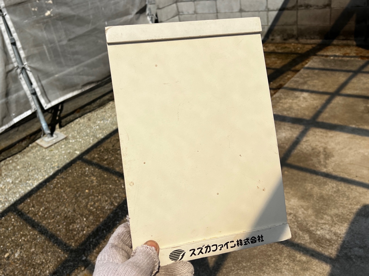 A4サイズの実際の「塗り板（色見本）」を太陽光の下で色味を最終確認している様子。面積が大きくなると色が明るく見える「面積効果」のズレを防ぐ、徳秀塗装がこだわる色選びの最終ステップです。