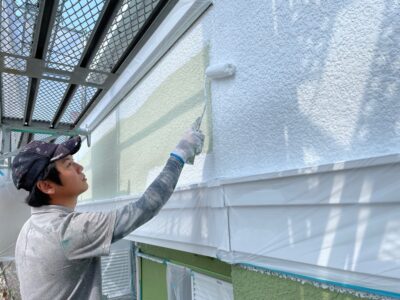 明石市・神戸市で活躍する外壁塗装店「徳秀塗装」の三男、徳山勇矢（とくやま ゆうや）が、ローラーを使って外壁を丁寧に塗り上げている真剣な施工風景