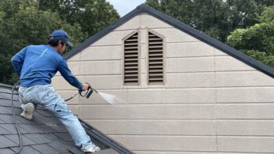 明石市・神戸市で外壁塗装を行う「徳秀塗装」の職人が、屋根の上で高圧洗浄機を使い、水しぶきを上げながら丁寧に外壁の汚れを落としている作業風景